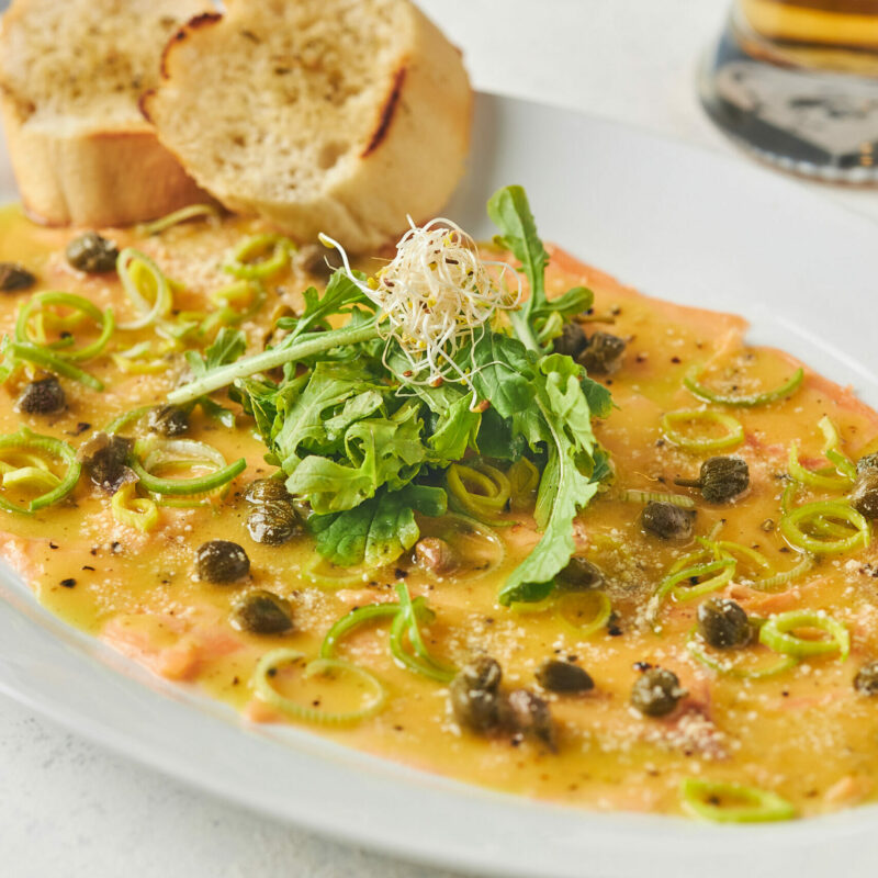 carpaccio de salmón con alcaparras, arúgula, alfalfa y vinagreta.